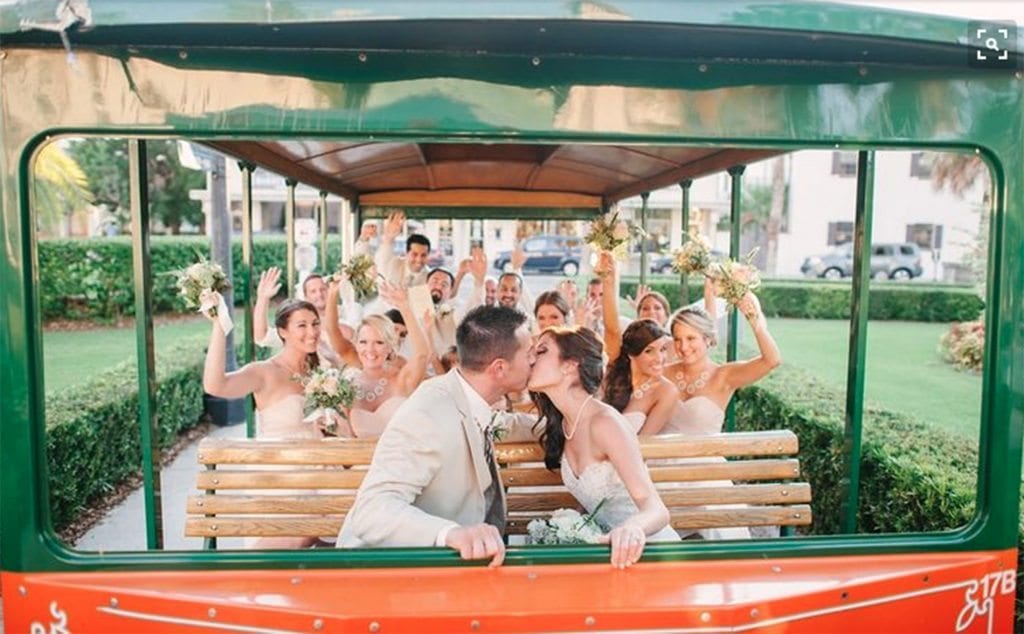 bridal party cheering as bride and groom kiss on Old Town Trolley after wedding ceremony at The Treasury on the Plaza