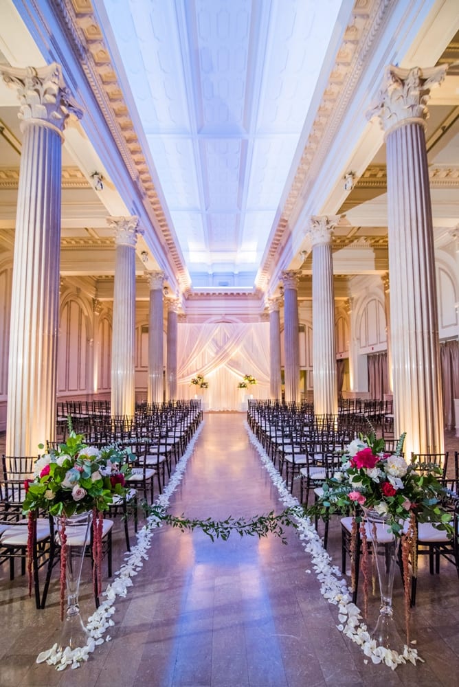 Flower petals line the aisle leading up to the white-draped wedding altar in the Treasury on the Plaza Grand Ballroom.