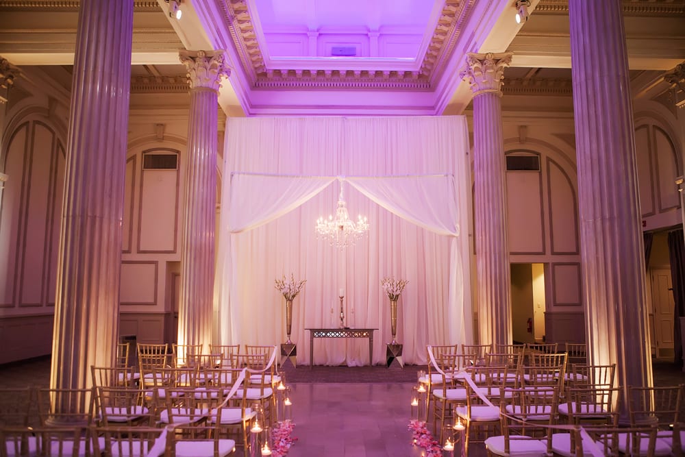 Candles and flowers line the aisle with a classic chandelier sitting over the altar during the wedding ceremony.
