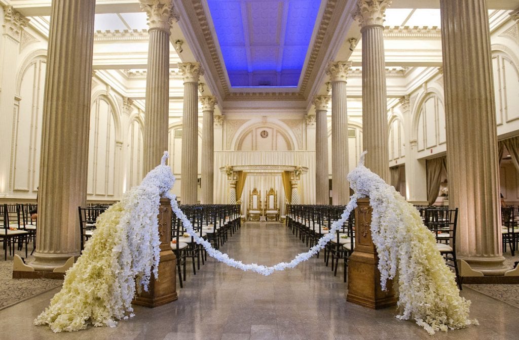 White flowers are arranged to make two peacocks that mark the start of the aisle for a traditional Indian wedding ceremony. 