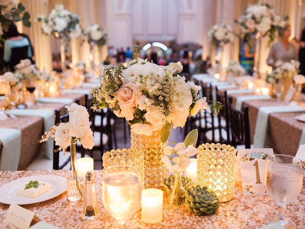 Floral arrangements from the wedding ceremony are used as table centerpieces during the reception in the same room.