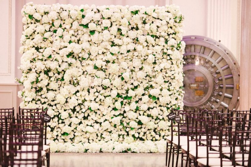 A floral wall of white flowers is the backdrop for this romantic wedding ceremony.