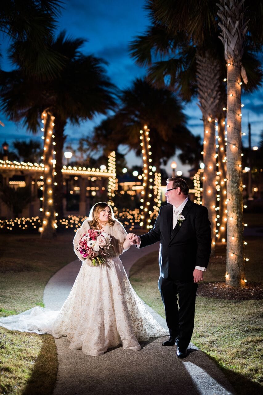 bride and groom walking outside with palm trees lit with holiday lights