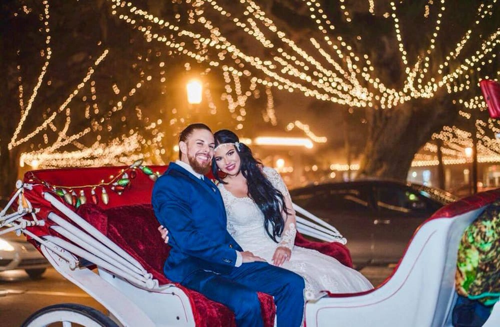 bride and groom in horse-drawn carriage with holiday lights behind them