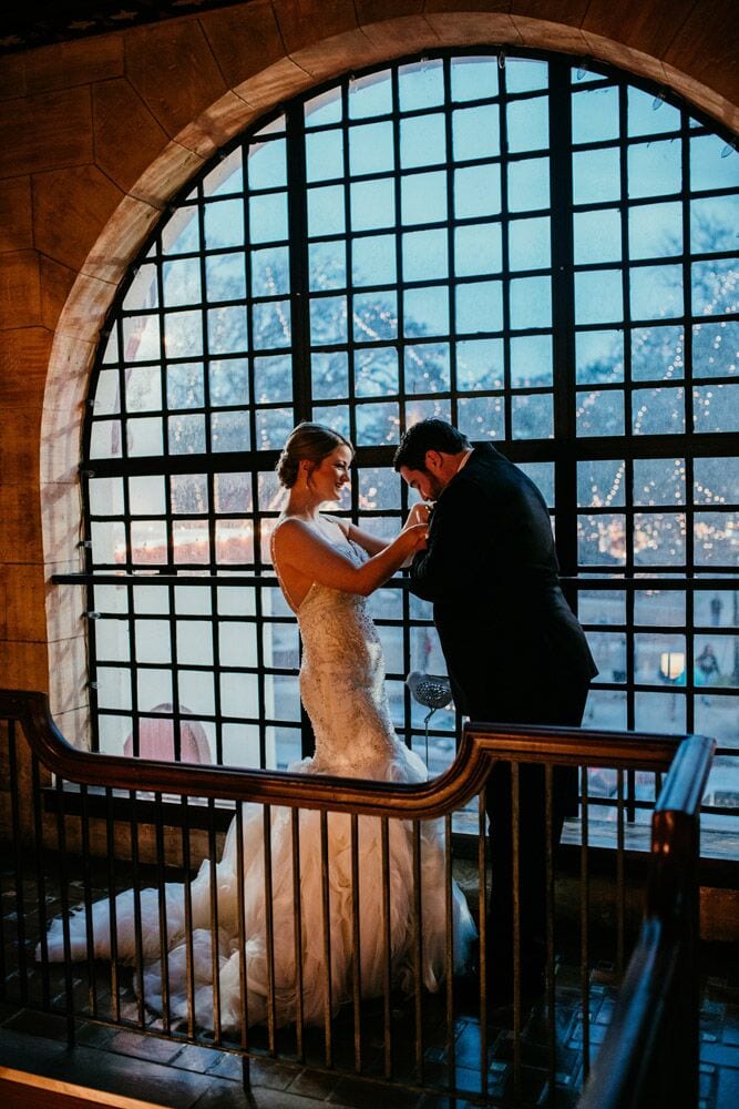 groom kissing bride's hand in front of window at Treasury on the Plaza