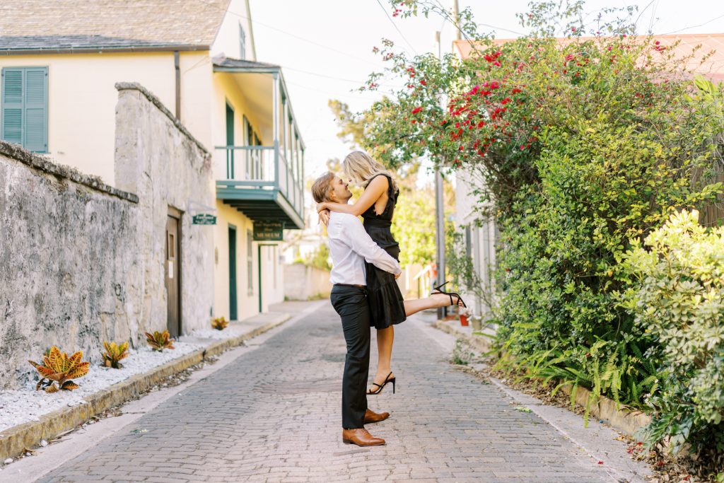 man lifting his fiancee during engagement photo shoot on cobblestone streets of St. Augustine