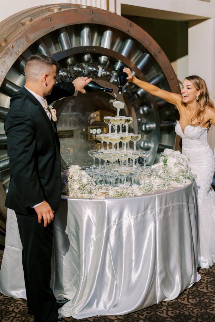 Hanna and Jared pouring champagne into a tower of glasses
