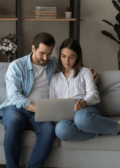 man and woman looking at laptop while sitting on couch
