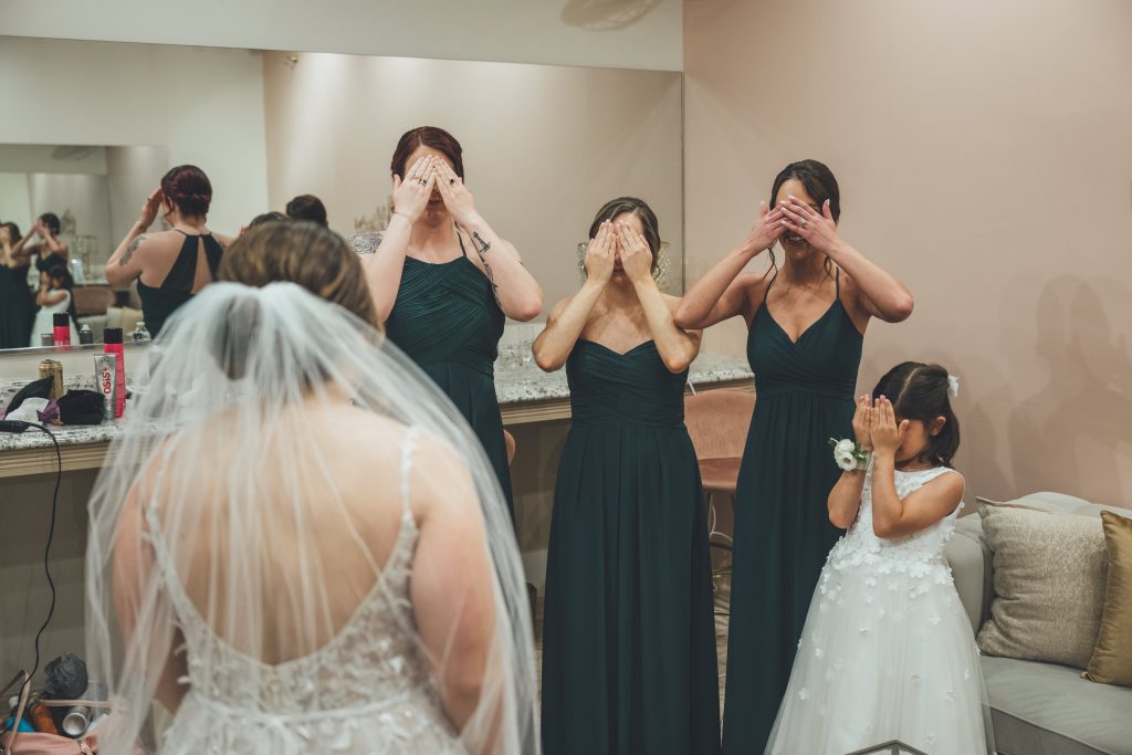Bride standing in front of bridesmaids who have their eyes covered